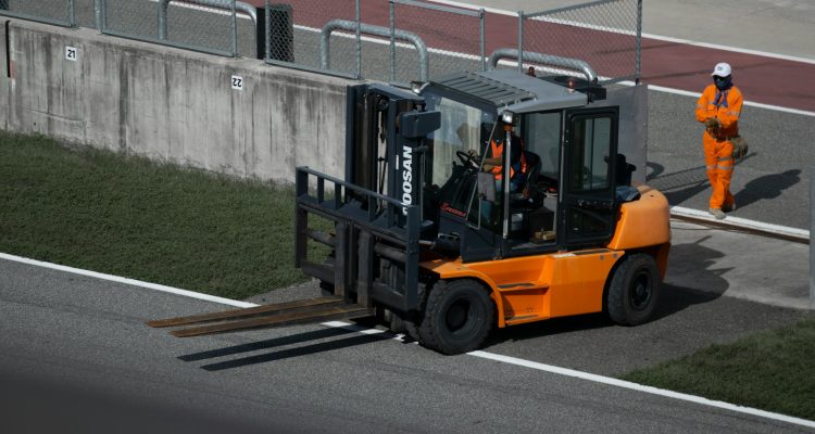 a forklift driving down a road next to a fence